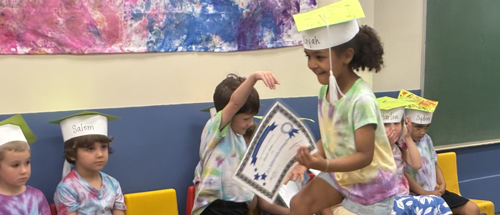 little girl in paper graduation cap walking across small stage