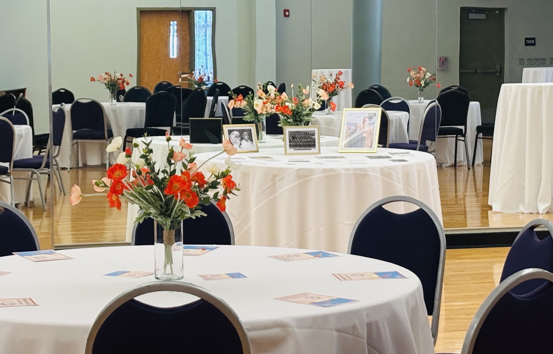 large room with hardwood floors and mirrors, set up with tables, chairs, and decor