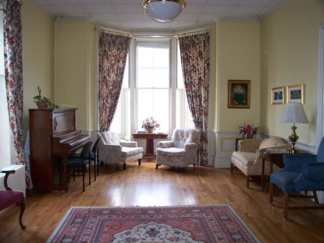 mid-sized room with hardwood floors, vintage furniture, a piano, and large windows