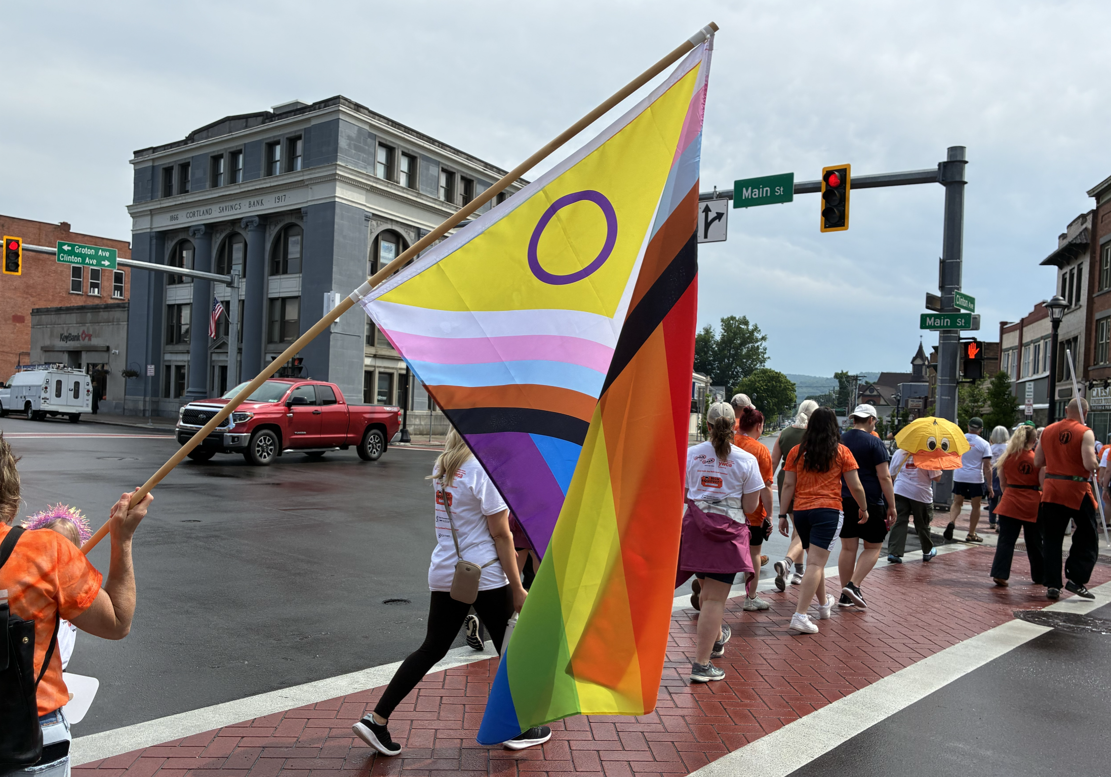 crossing guard waving a pride flag while a group of people crosses the street
